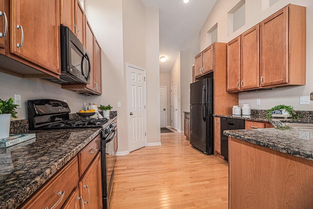 kitchen featuring brown cabinetry, dark stone countertops, high vaulted ceiling, light wood-type flooring, and black appliances