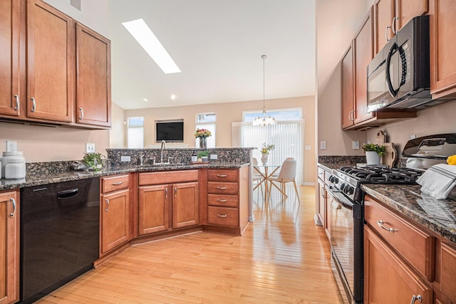 kitchen with a sink, a peninsula, a chandelier, black appliances, and light wood-type flooring