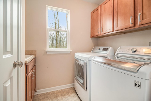 clothes washing area featuring washing machine and clothes dryer, baseboards, and cabinet space