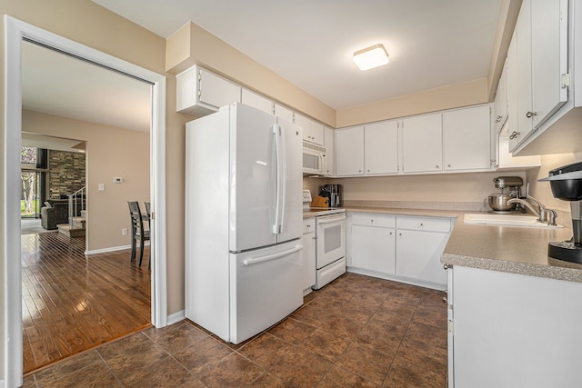kitchen with a sink, white appliances, white cabinetry, light countertops, and baseboards