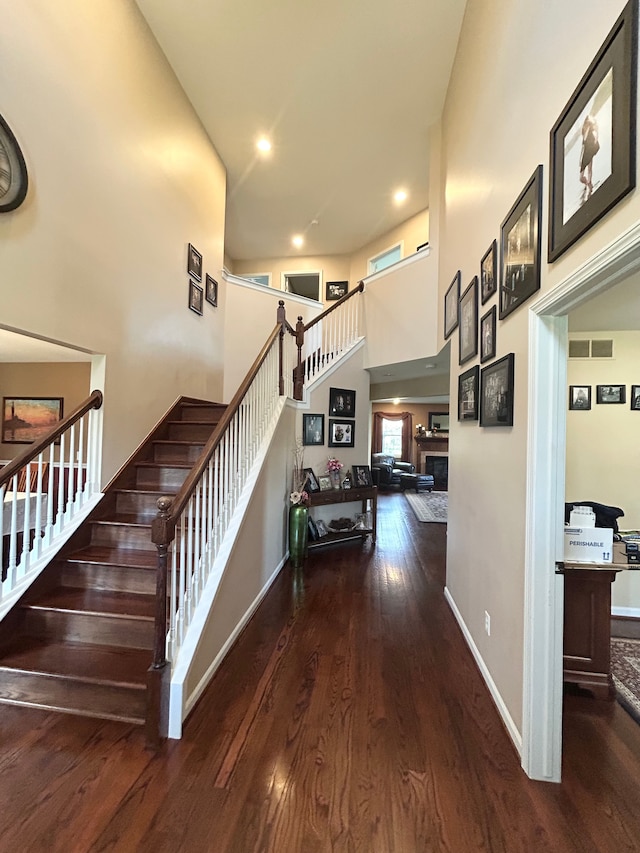 stairs with baseboards, wood finished floors, a towering ceiling, and a fireplace