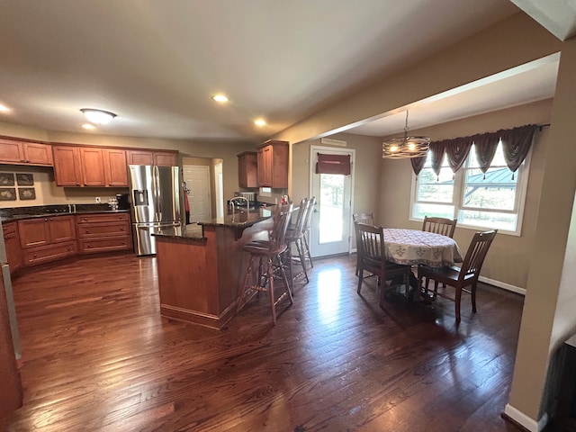 kitchen with brown cabinetry, recessed lighting, dark wood-style flooring, a kitchen bar, and stainless steel fridge with ice dispenser