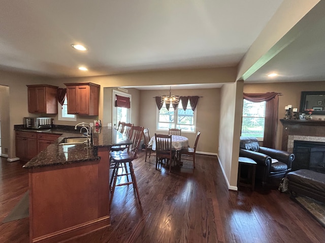 kitchen with brown cabinetry, dark wood finished floors, a sink, a kitchen bar, and dark stone countertops
