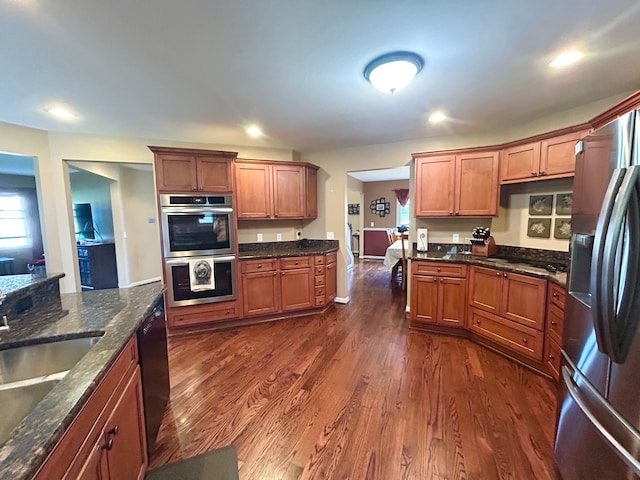 kitchen featuring brown cabinetry, stainless steel appliances, a sink, and dark wood-type flooring