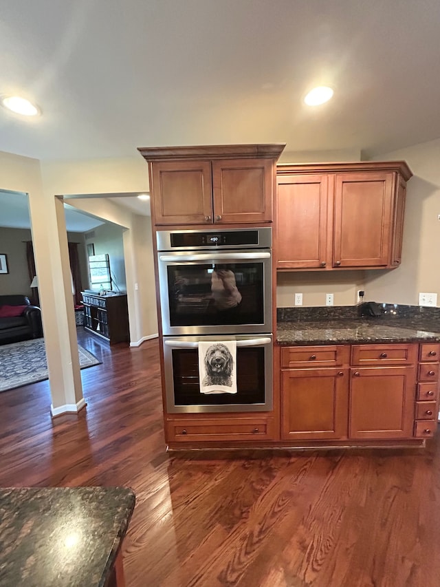 kitchen featuring dark stone counters, dark wood finished floors, stainless steel double oven, and brown cabinetry