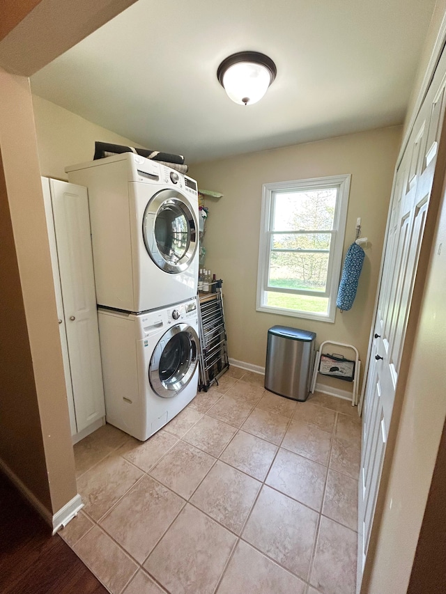laundry room featuring stacked washing maching and dryer, laundry area, baseboards, and light tile patterned floors