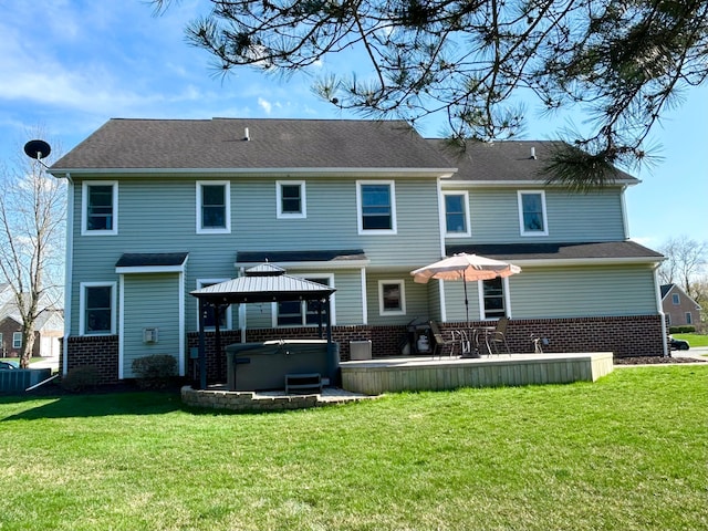 back of property featuring a hot tub, a gazebo, a yard, and brick siding