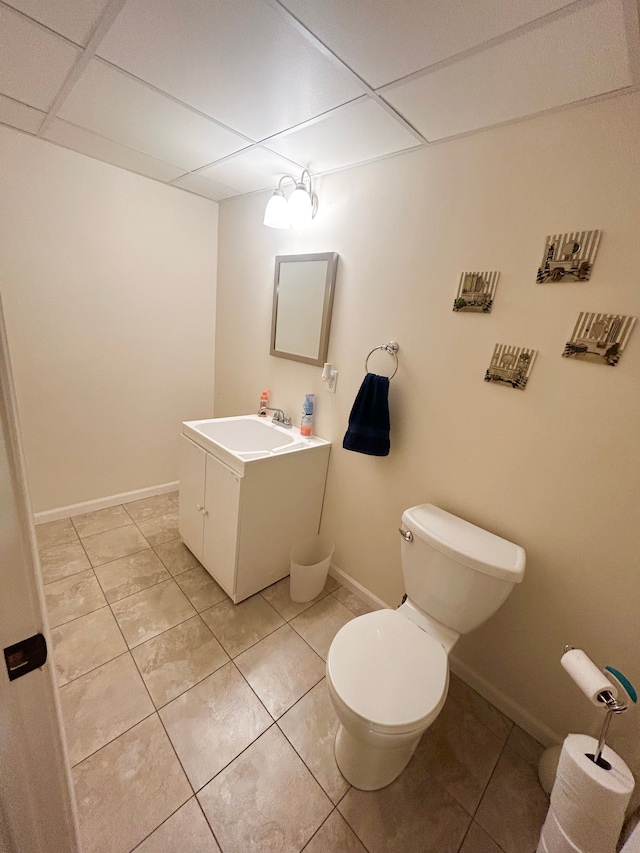 bathroom featuring a drop ceiling, toilet, baseboards, tile patterned flooring, and vanity