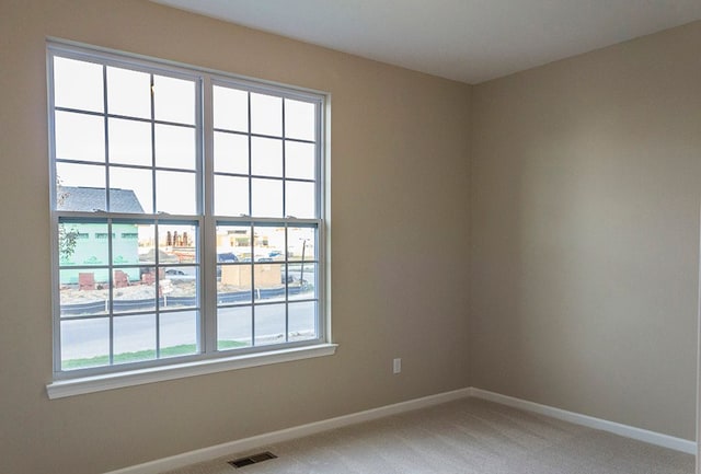 unfurnished room featuring light colored carpet, plenty of natural light, visible vents, and baseboards