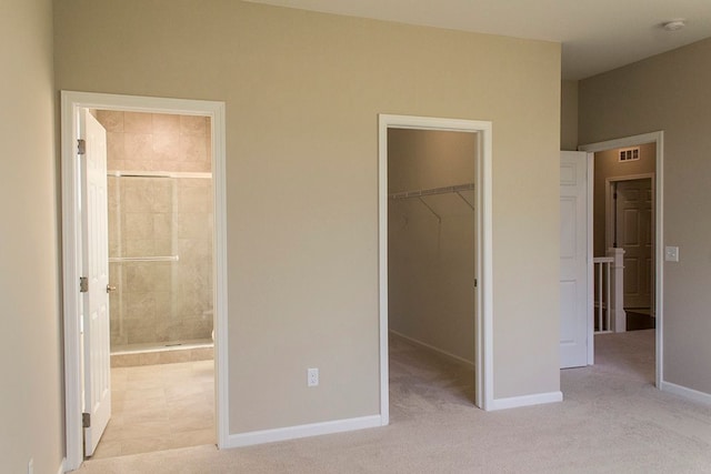 unfurnished bedroom featuring a walk in closet, light carpet, and visible vents