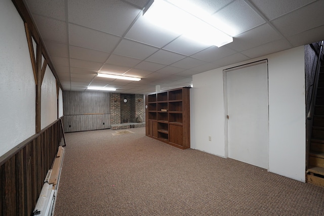finished below grade area with a paneled ceiling, carpet flooring, wooden walls, and a fireplace