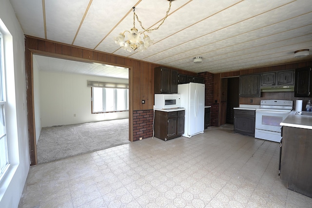 kitchen featuring wood walls, white appliances, under cabinet range hood, an inviting chandelier, and light countertops