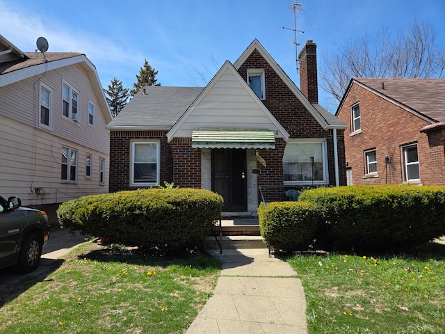 bungalow featuring a chimney, a front yard, and brick siding