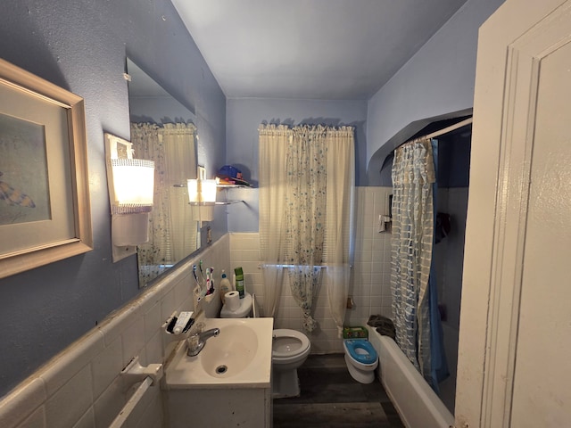 bathroom with toilet, tile walls, wood finished floors, shower / tub combo with curtain, and a wainscoted wall