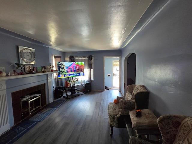 living room featuring a fireplace with flush hearth, arched walkways, and dark wood-style floors