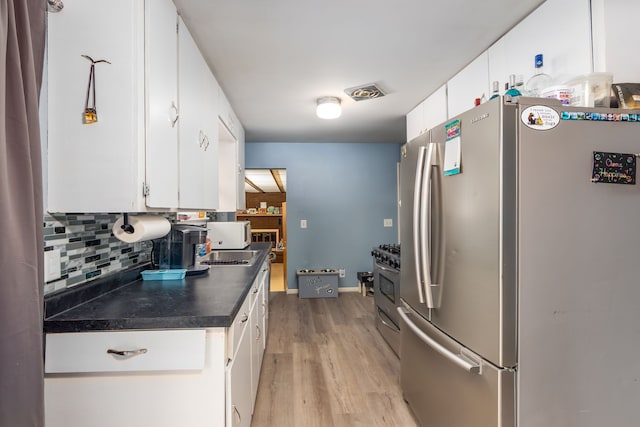 kitchen with appliances with stainless steel finishes, decorative backsplash, light wood finished floors, dark countertops, and white cabinetry
