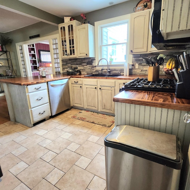 kitchen with glass insert cabinets, butcher block counters, a sink, backsplash, and stainless steel appliances