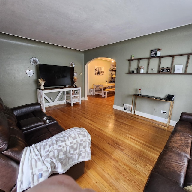 living area featuring arched walkways, baseboards, visible vents, and wood finished floors