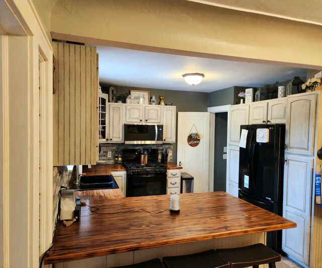 kitchen with wooden counters, a sink, a peninsula, black appliances, and tasteful backsplash
