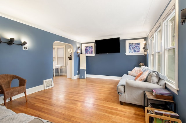 living area featuring arched walkways, baseboards, light wood-style flooring, and visible vents