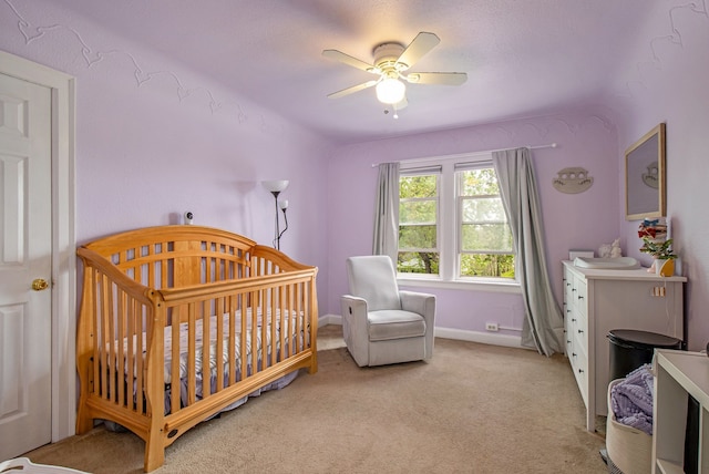 bedroom featuring a crib, baseboards, a ceiling fan, and light colored carpet