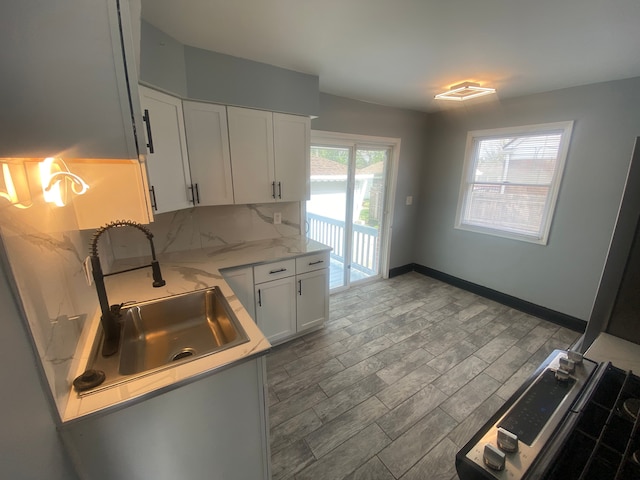 kitchen featuring a sink, wood finish floors, light stone counters, white cabinetry, and backsplash