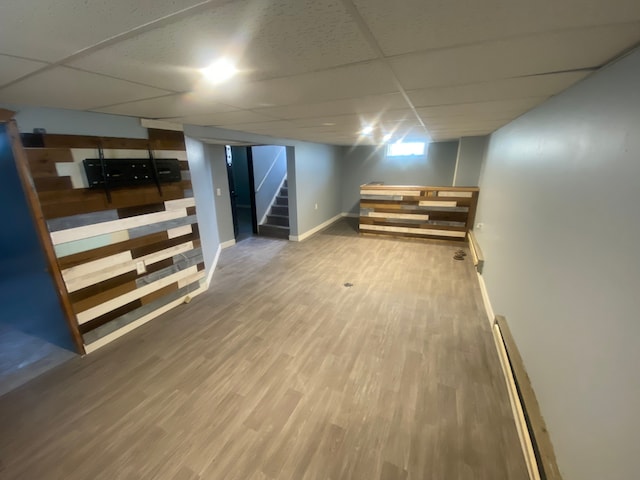 finished basement featuring stairs, wood finished floors, a baseboard heating unit, and a drop ceiling