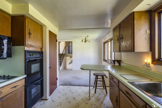 kitchen with brown cabinets, a sink, black appliances, light countertops, and light carpet