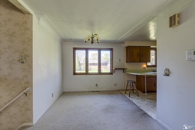 unfurnished dining area featuring baseboards, an inviting chandelier, visible vents, and light colored carpet