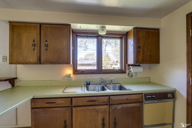 kitchen featuring dishwasher, light countertops, brown cabinetry, and a sink