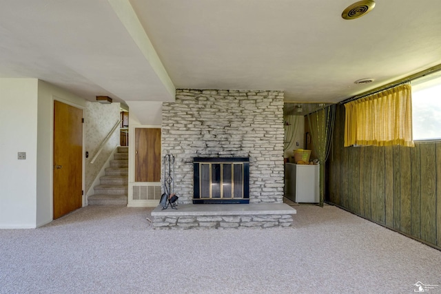 unfurnished living room featuring carpet flooring, a stone fireplace, visible vents, and stairway