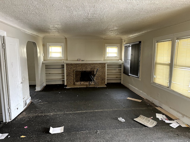 unfurnished living room featuring arched walkways, a premium fireplace, and a textured ceiling