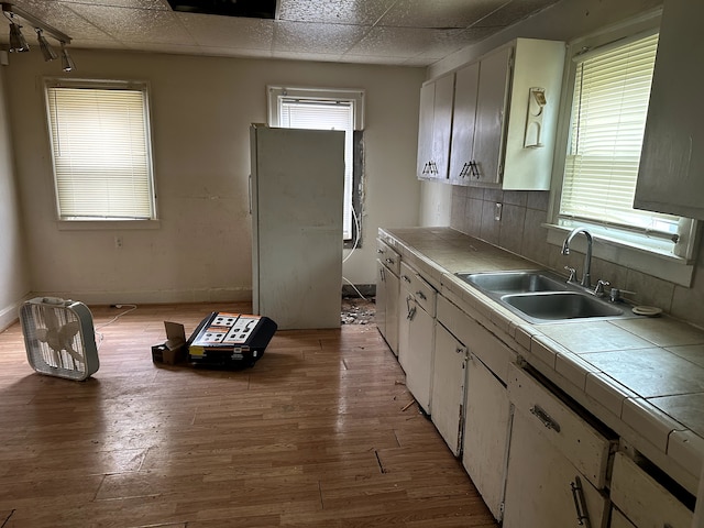 kitchen featuring light wood-style flooring, a sink, decorative backsplash, tile counters, and white cabinets