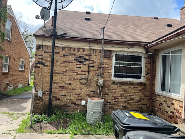 view of property exterior featuring brick siding, central AC unit, and roof with shingles