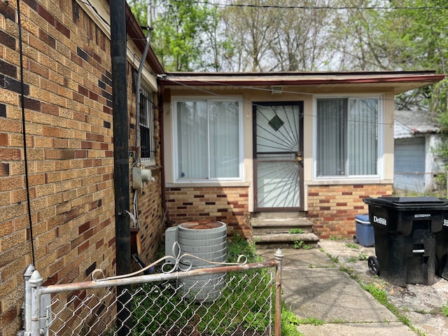 property entrance featuring brick siding, fence, and central AC
