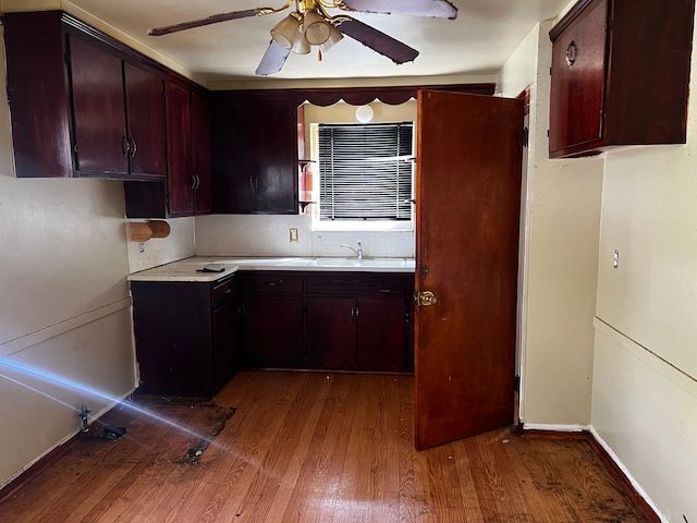 kitchen with wood finished floors, ceiling fan, light countertops, baseboards, and a sink