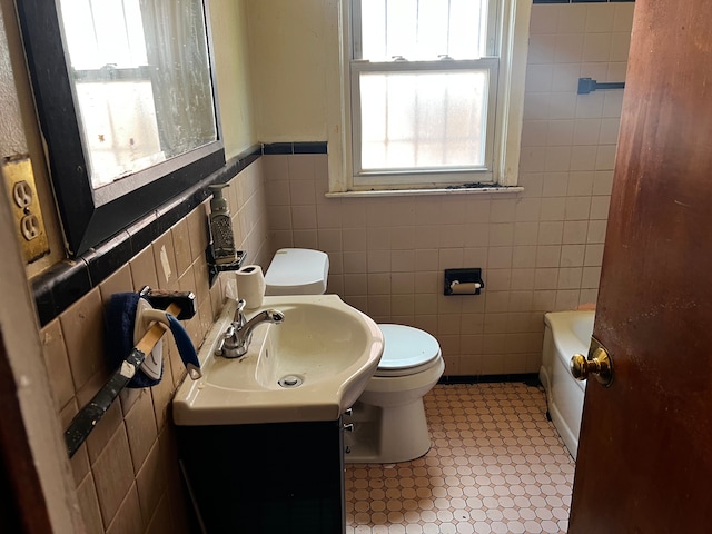 bathroom featuring tile walls, toilet, a bathtub, vanity, and a wainscoted wall