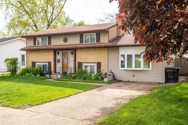 tri-level home with brick siding, a chimney, and a front lawn