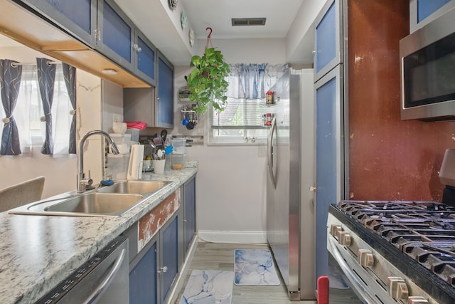 kitchen featuring blue cabinets, appliances with stainless steel finishes, a sink, and light wood finished floors