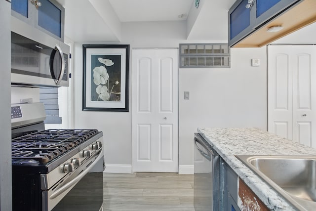 kitchen featuring stainless steel appliances, blue cabinets, light countertops, light wood-style floors, and baseboards
