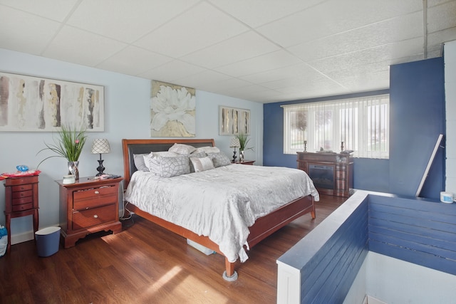 bedroom featuring a drop ceiling, wood finished floors, and a fireplace