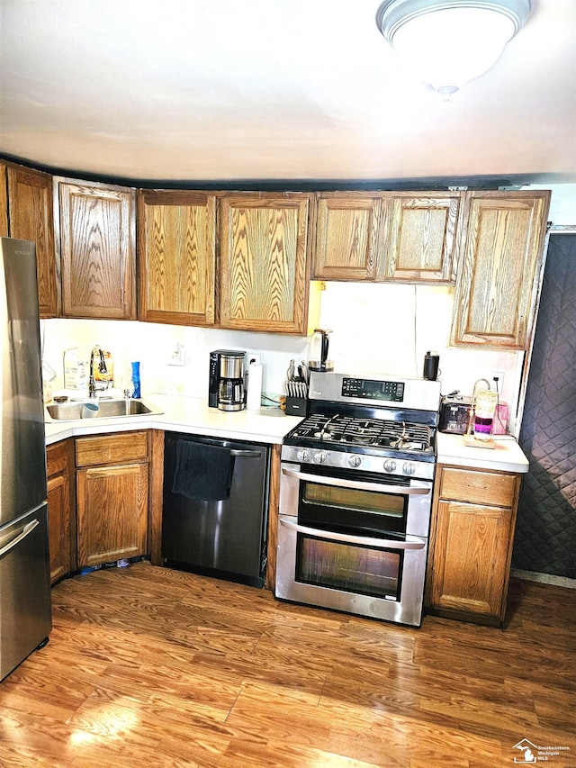 kitchen with a sink, stainless steel appliances, light countertops, and wood finished floors
