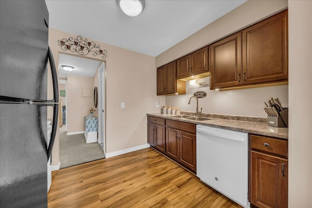 kitchen featuring a sink, freestanding refrigerator, dishwasher, light wood finished floors, and baseboards