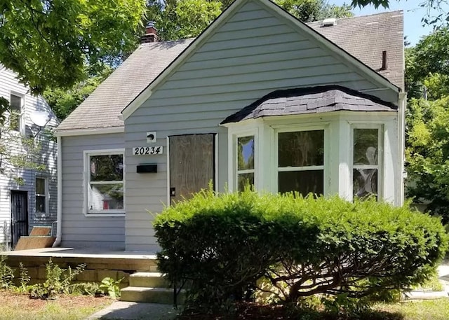 bungalow-style house with covered porch, roof with shingles, and a chimney
