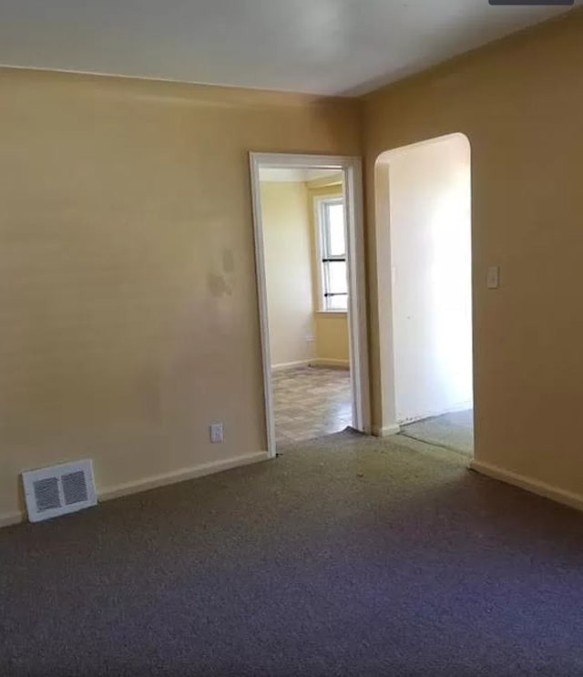 carpeted empty room featuring arched walkways, baseboards, and visible vents