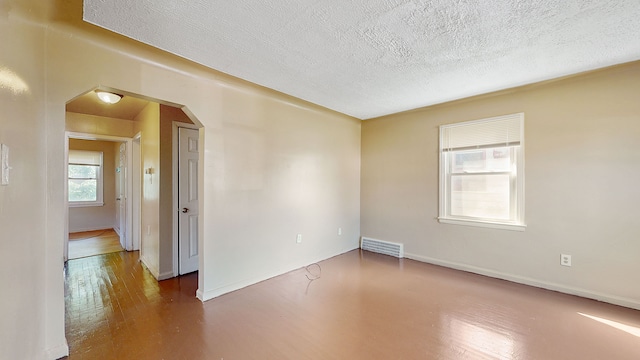 empty room featuring wood finished floors, a textured ceiling, visible vents, arched walkways, and baseboards
