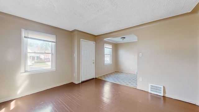 foyer entrance featuring baseboards, visible vents, a textured ceiling, and arched walkways
