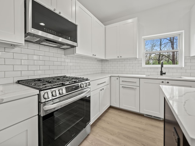 kitchen featuring appliances with stainless steel finishes, white cabinetry, light stone countertops, and backsplash