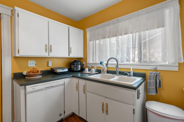 kitchen featuring white dishwasher, dark countertops, white cabinets, and a sink