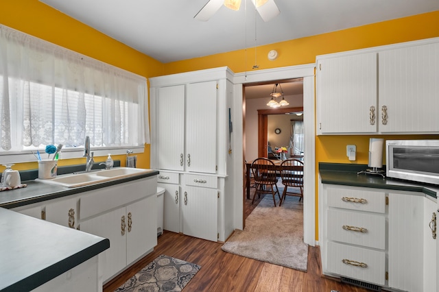 kitchen featuring a sink, stainless steel microwave, dark wood finished floors, white cabinetry, and a ceiling fan